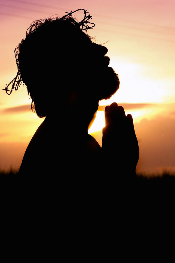 A silhouette of a man praying at sunset, wearing a crown of thorns, symbolizing faith and hope.