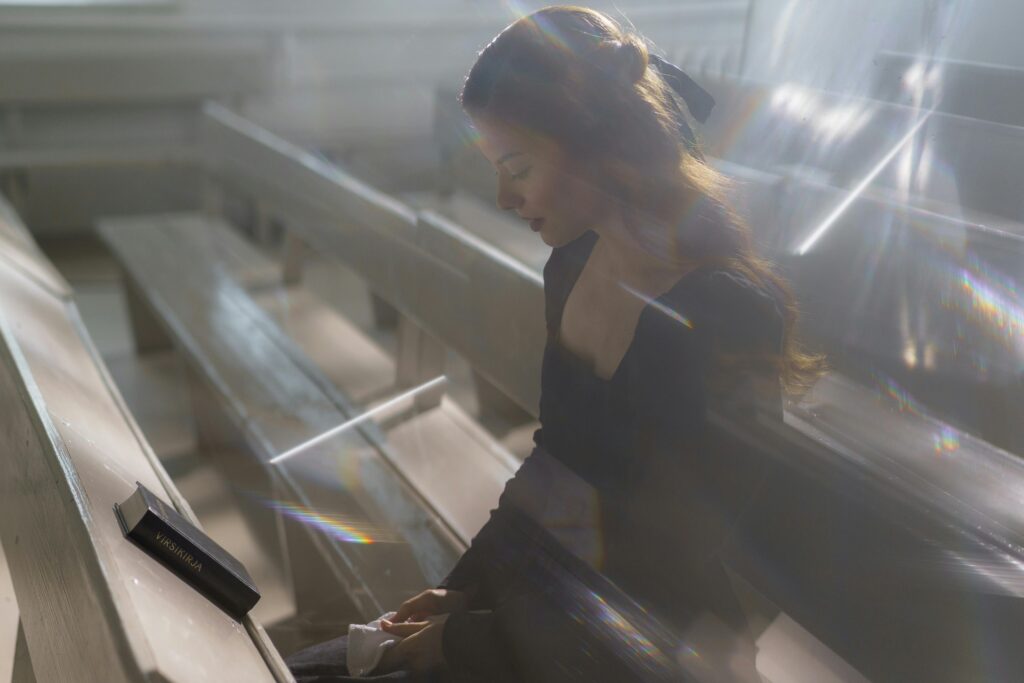 A woman sits alone in pews, lost in thought, surrounded by ethereal light.