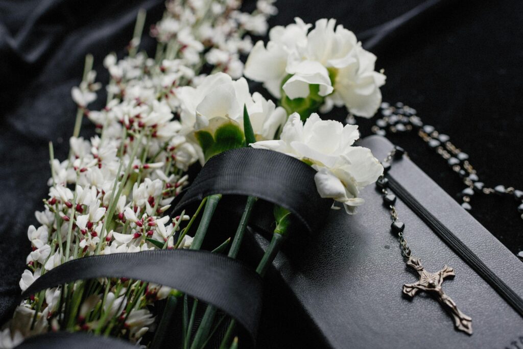 Close-up of white flowers and rosary on dark cloth, symbolizing mourning and spirituality.